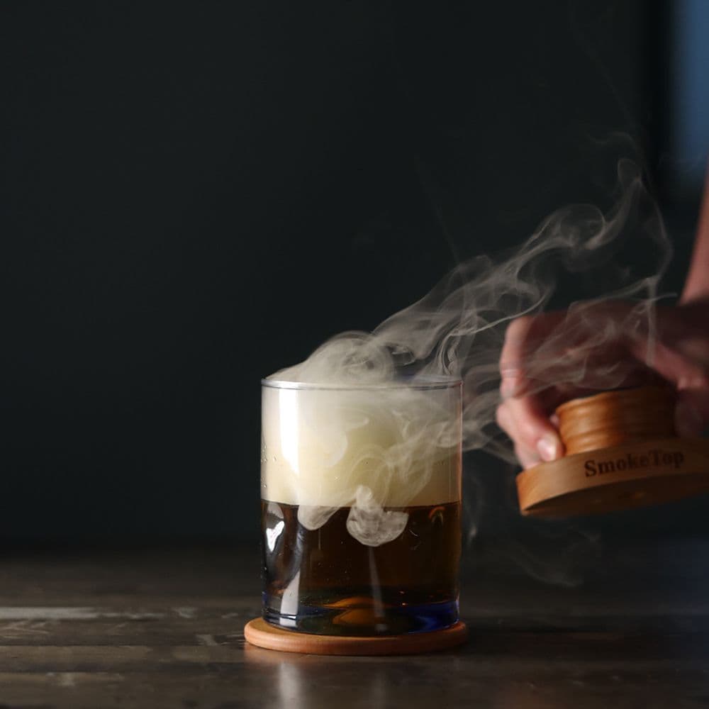 Smoke curling from a SmokeTop into a craft cocktail on a bar top